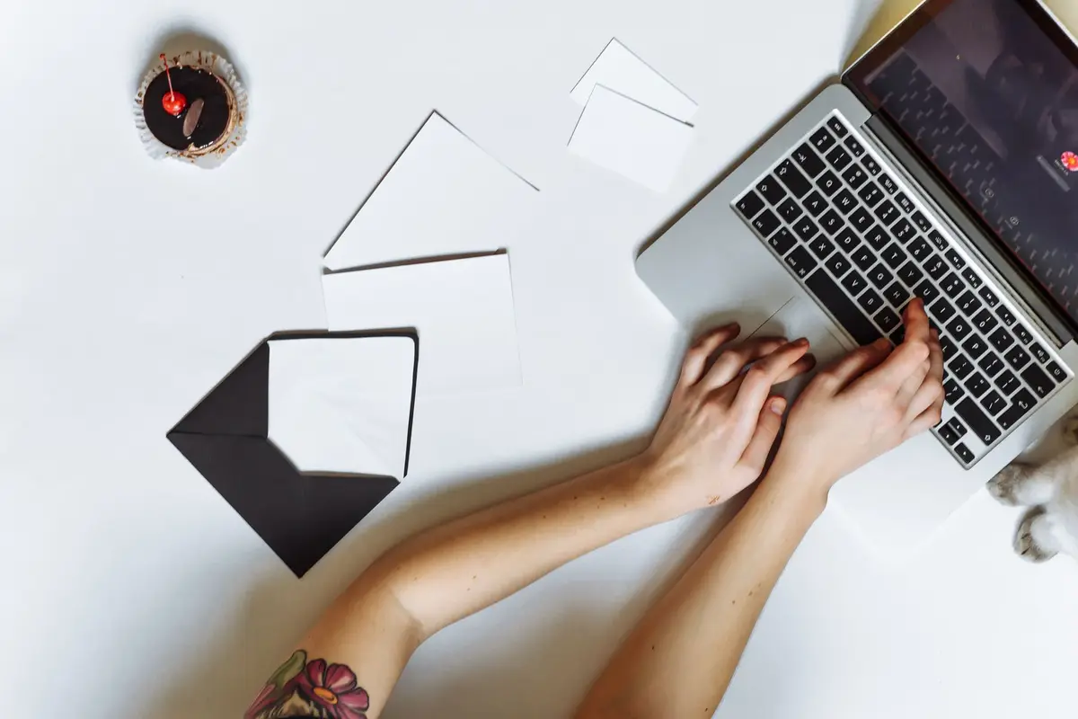 Hands typing on a laptop beside an open envelope and a small card
