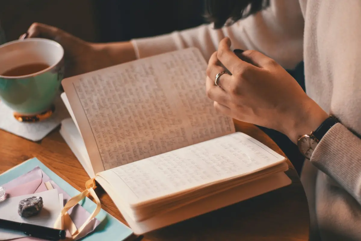 Someone writing in an open journal beside a cup of tea