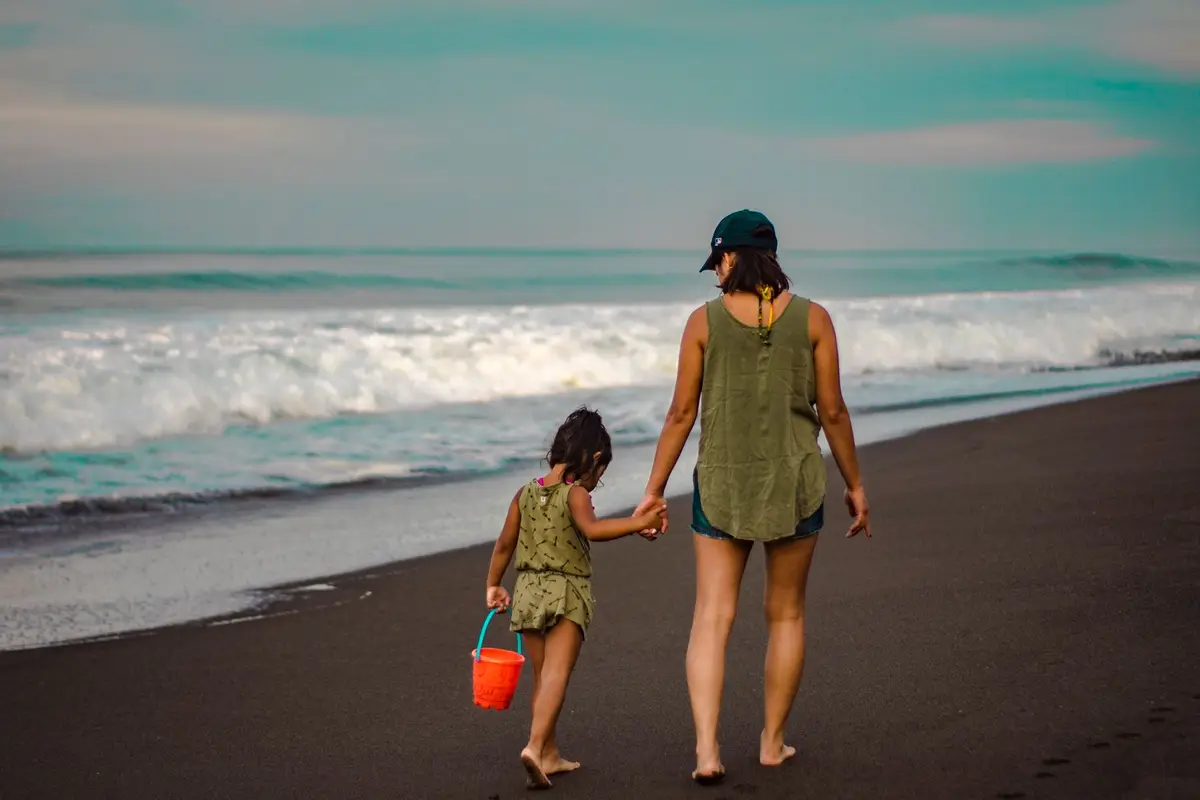 A mother and her young daughter walking along the shore