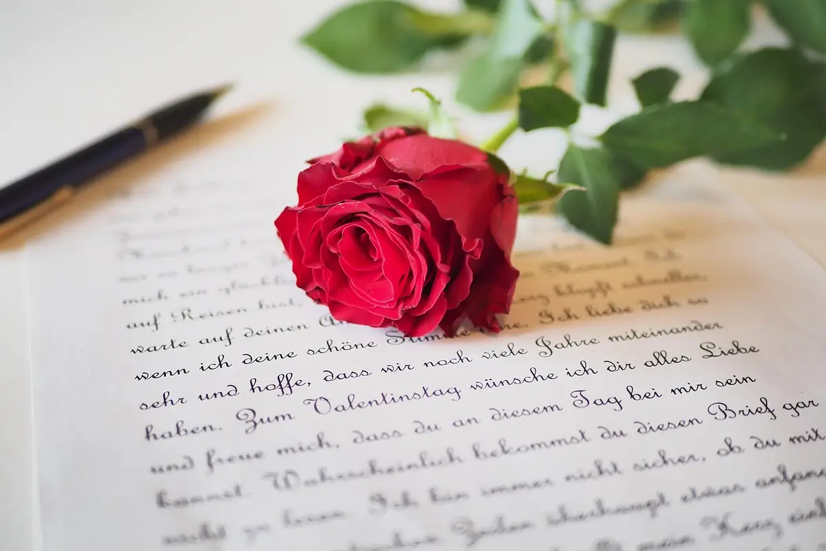 A red rose lying on a handwritten love letter beside a pen