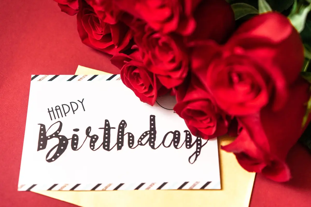A handwritten Happy Birthday card beside red roses