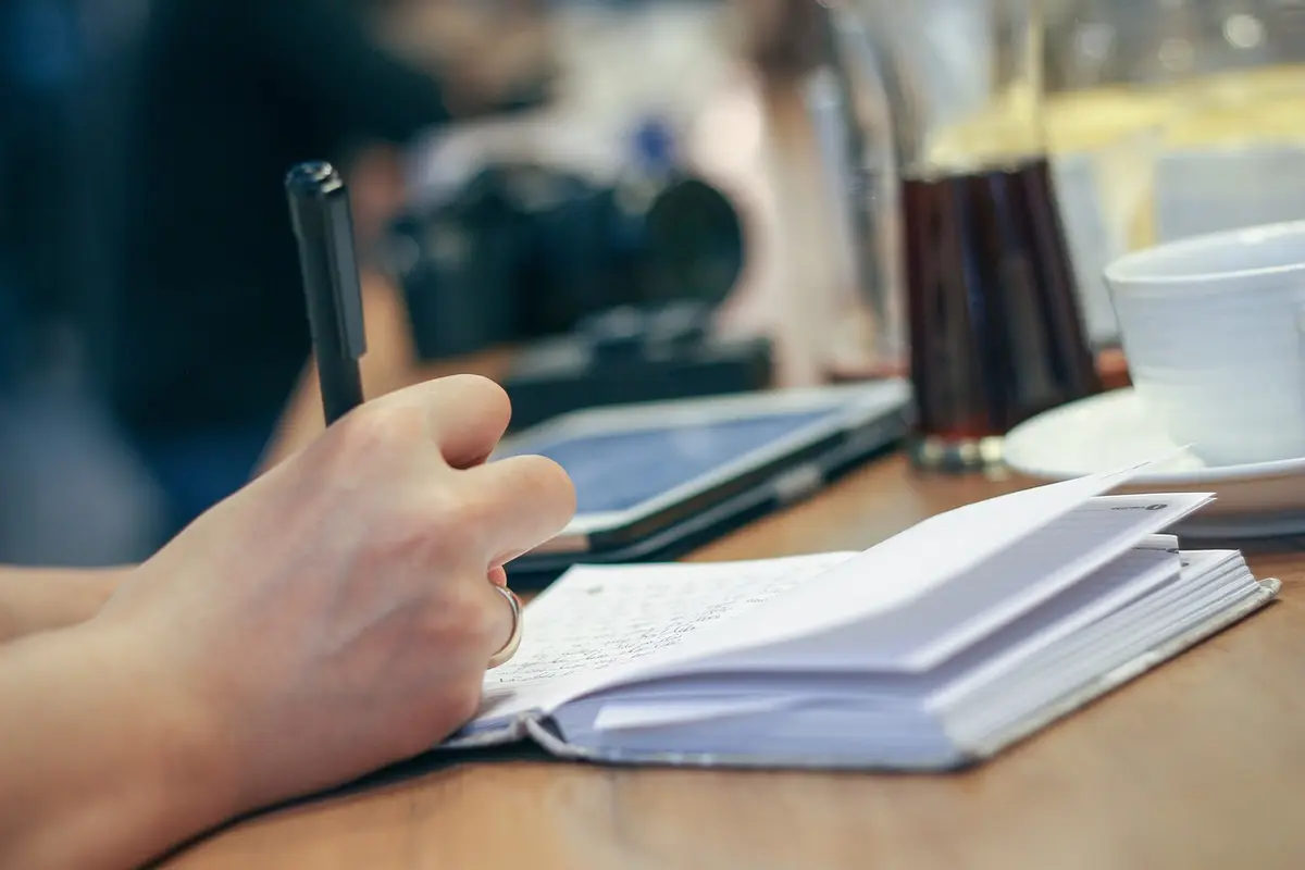 A hand writing in a small notebook at a desk