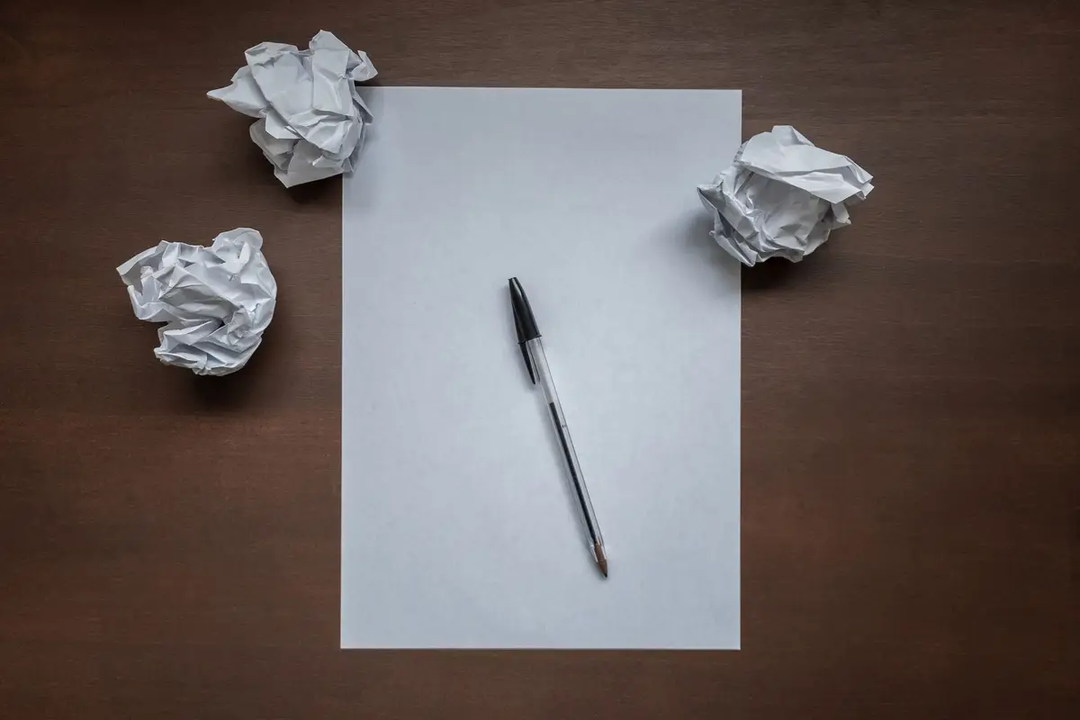 A blank sheet of paper and a pen among crumpled drafts