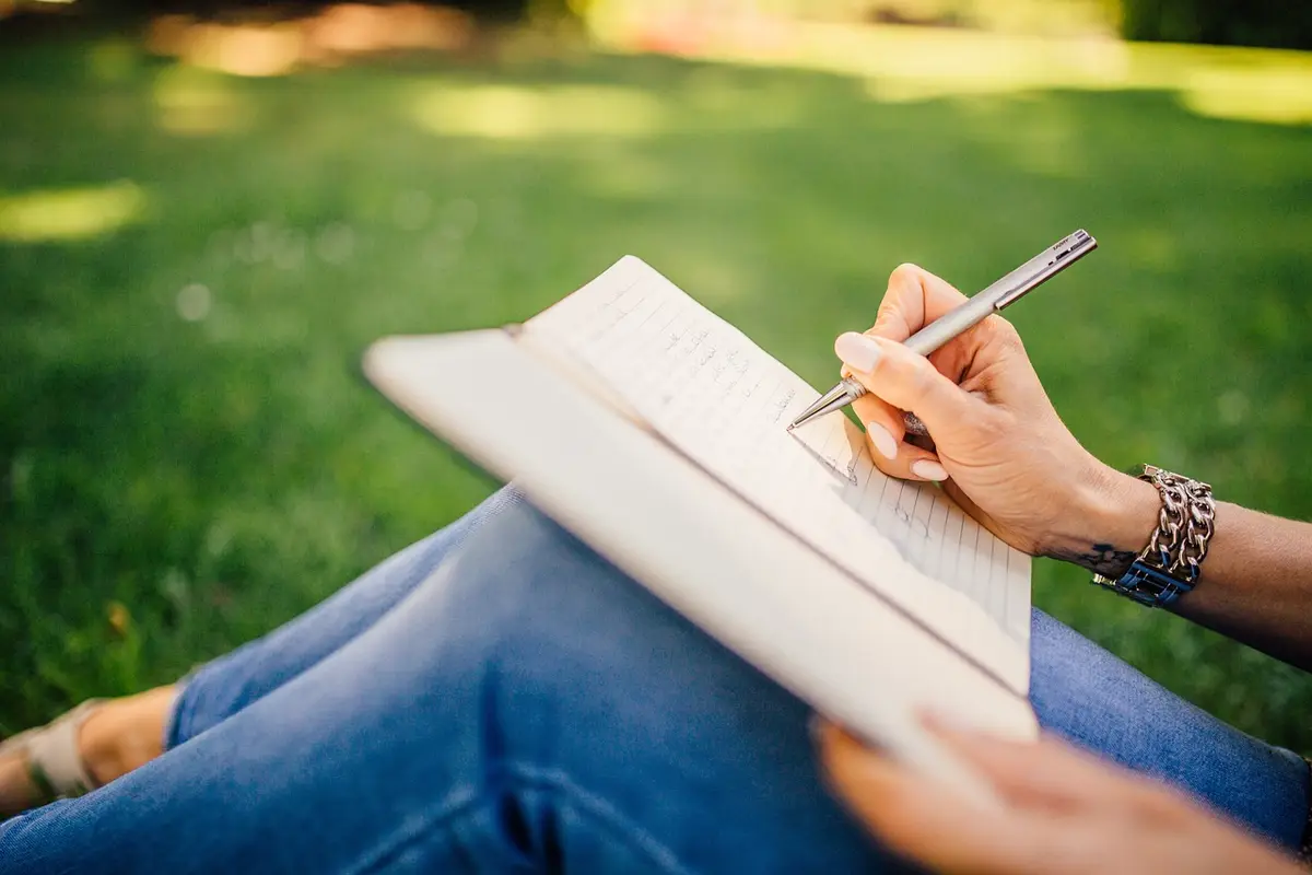 Someone writing in a notebook while sitting on the grass